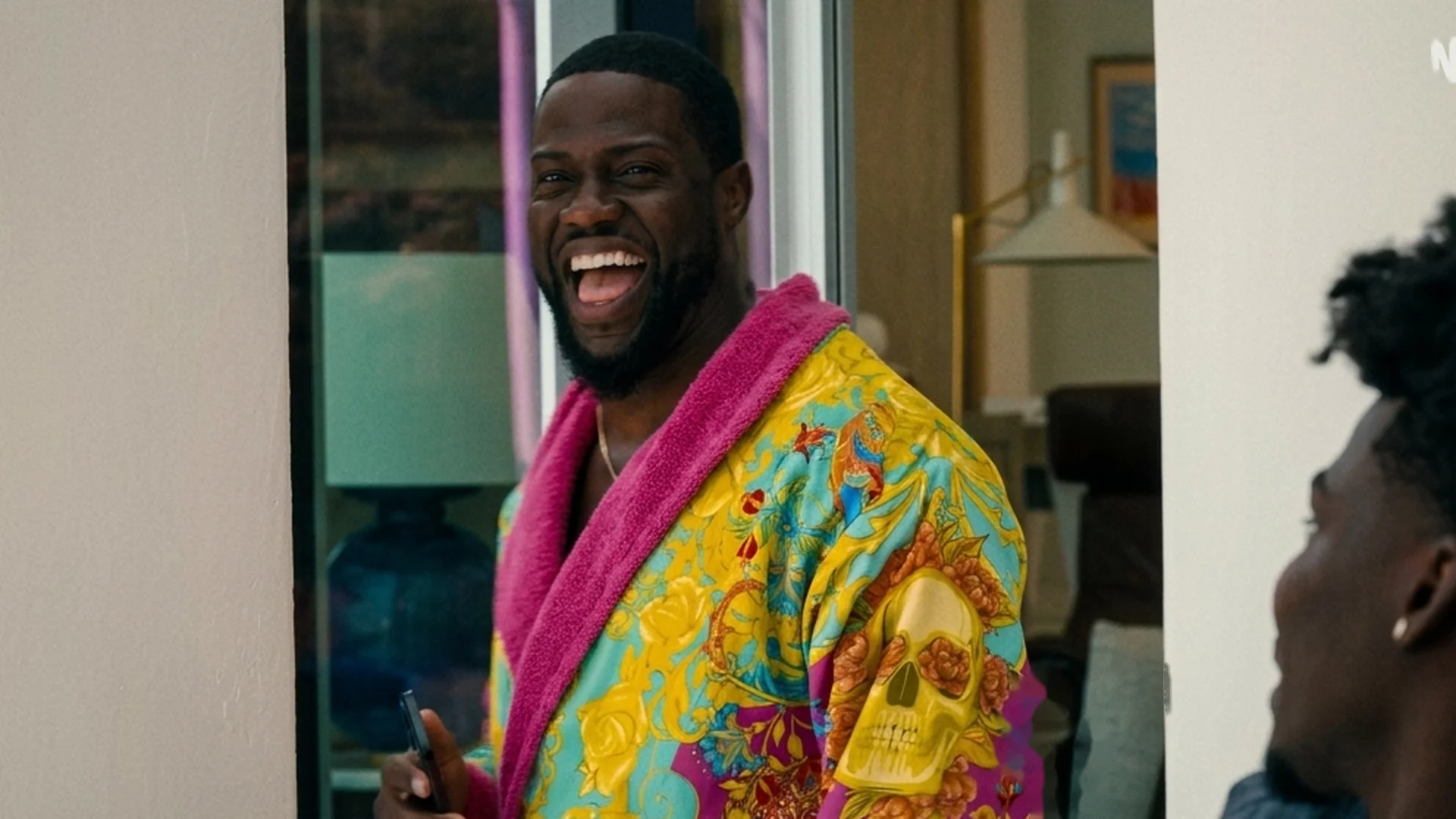 Kevin Hart laughs in a bright, colorful robe as a younger man looks on in 72 Hours