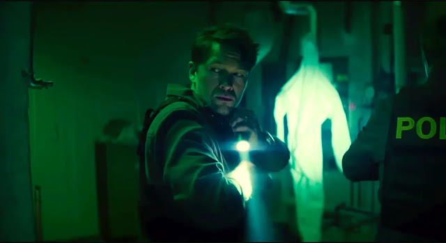 Thomas Berg (Jakob Oftebro) with a flashlight faces a police officer in a green-lit corridor in Blood Sacrifice