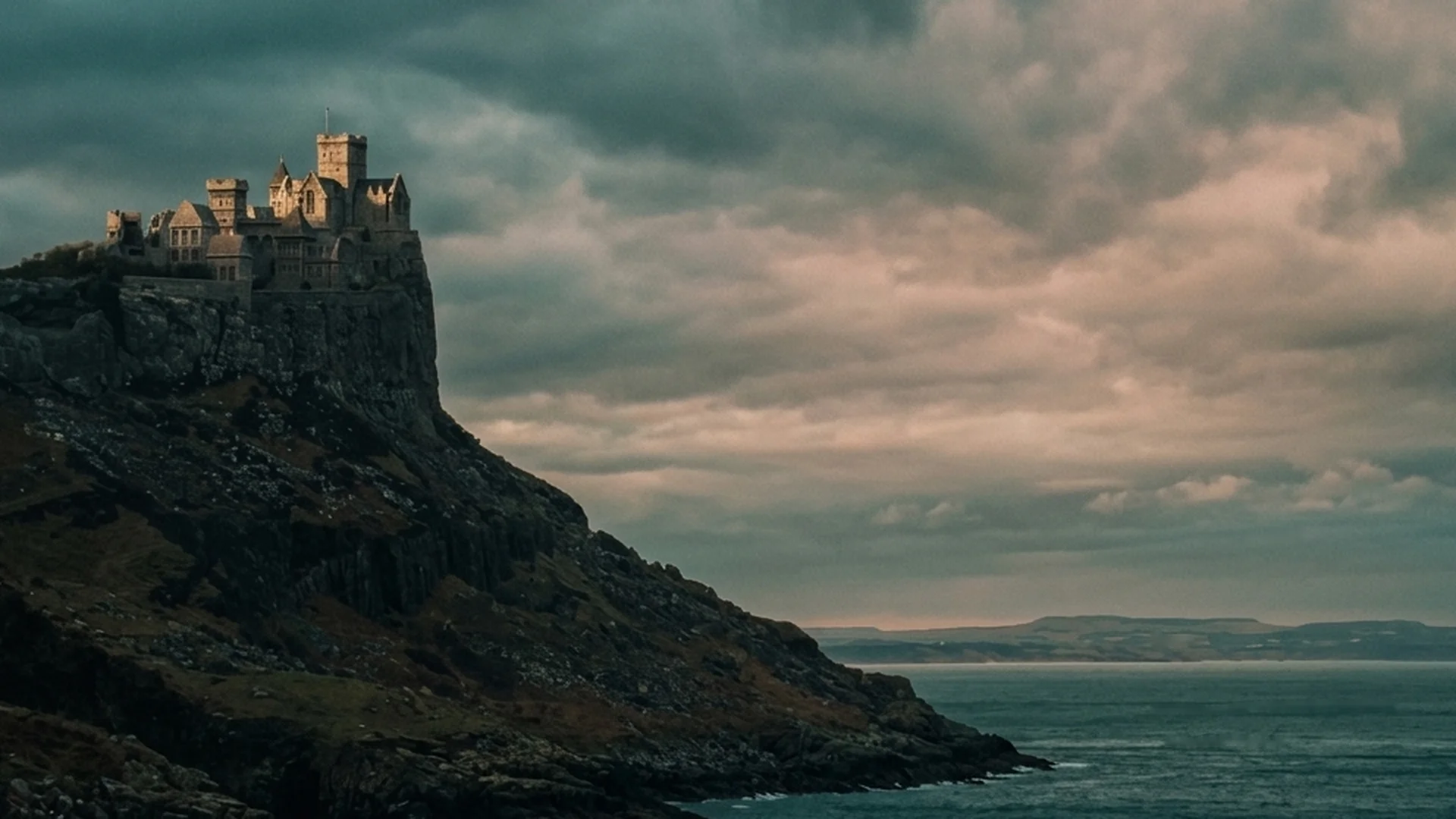 A stone castle sits on a high cliff above the sea at dusk.
