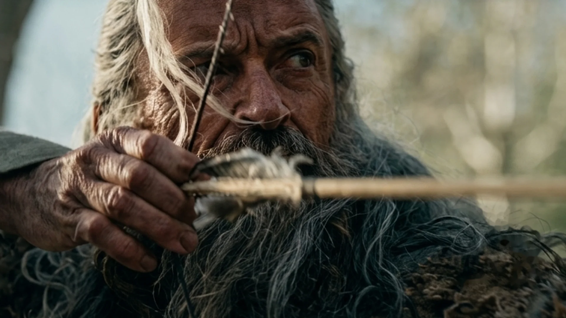 Hugh Jackman, in a fur cloak, draws a longbow and takes aim.