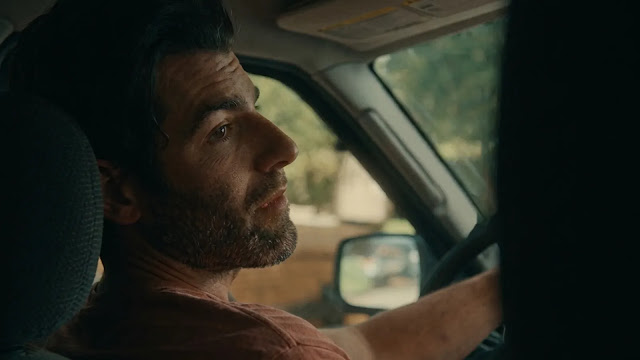 A man driving alone, looking drawn and tired
