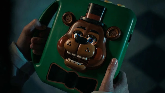 A child's hands hold a green Freddy Fazbear toy in the Five Nights at Freddy's 2 trailer