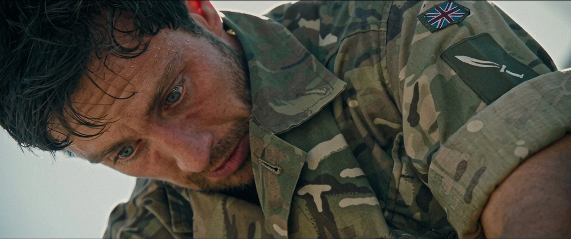 Major Will Tranter (Aaron Taylor-Johnson) pressed flat to the ground in army fatigues, sweating, in Fuze