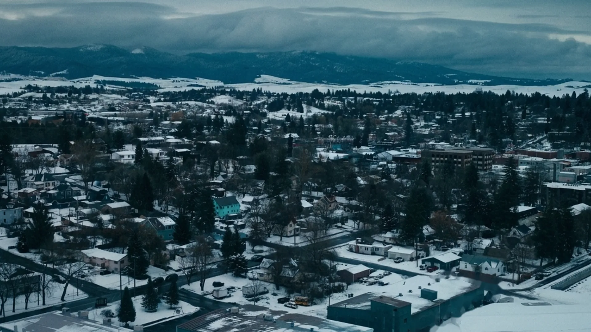 An aerial view of a snow-covered small town under a gray winter sky.