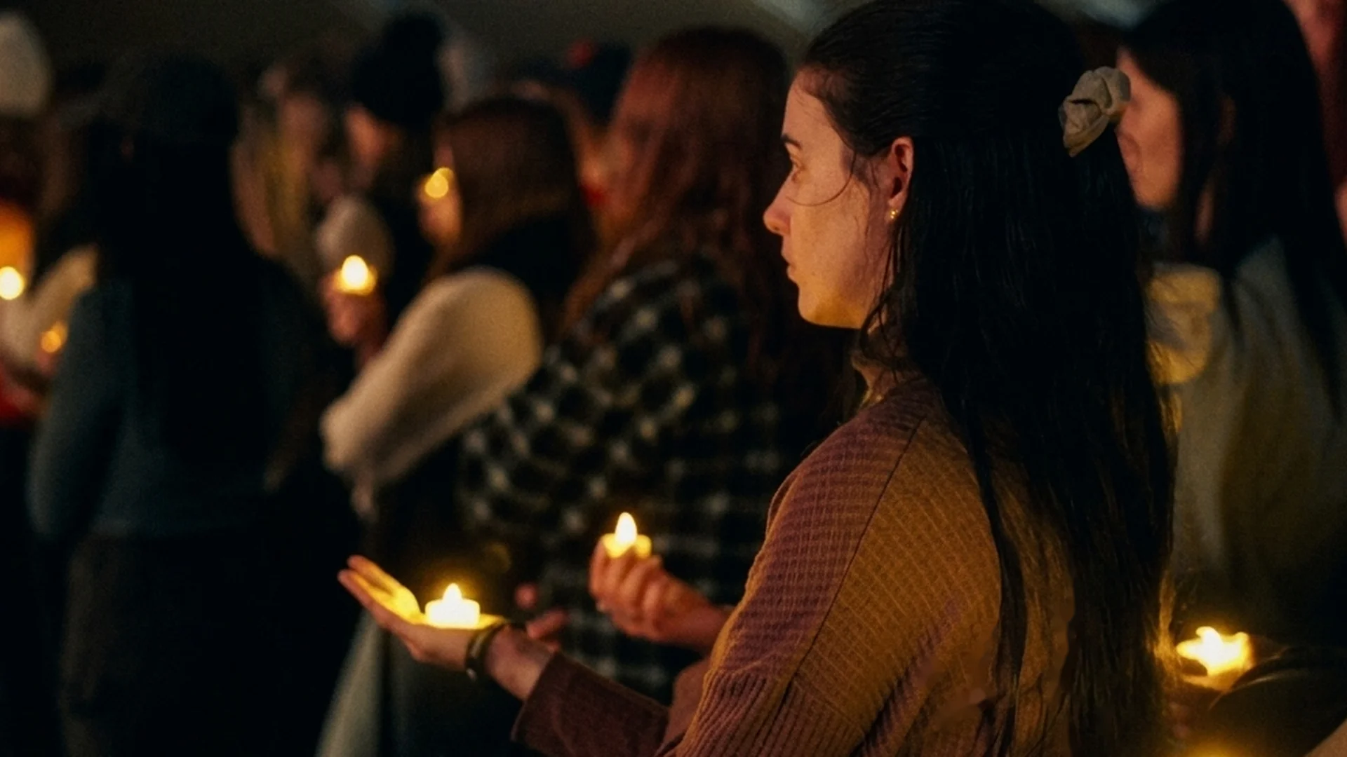 Students hold lit candles close together at an outdoor vigil at night.