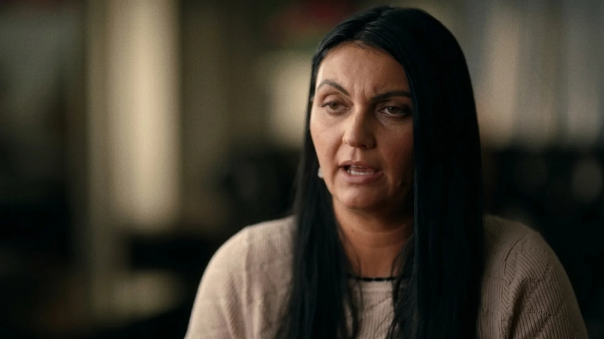 A woman with long dark hair speaks during a sit-down interview.
