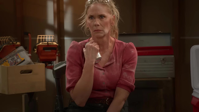 A woman alone in a garage in Leanne, holding a flashlight against her chest and looking off with a worried expression