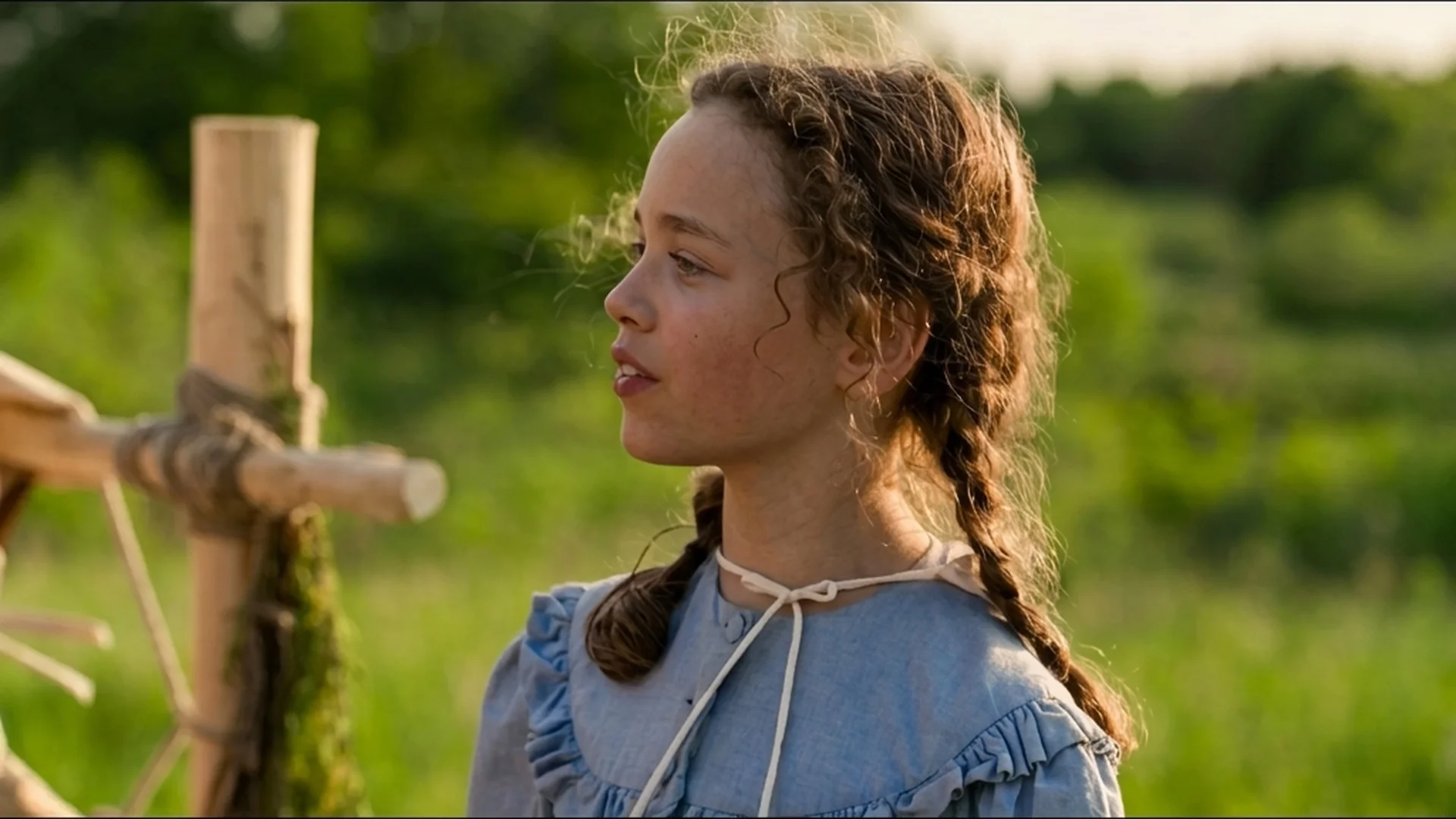 A girl with braided hair stands beside a wooden fence in Little House on the Prairie.
