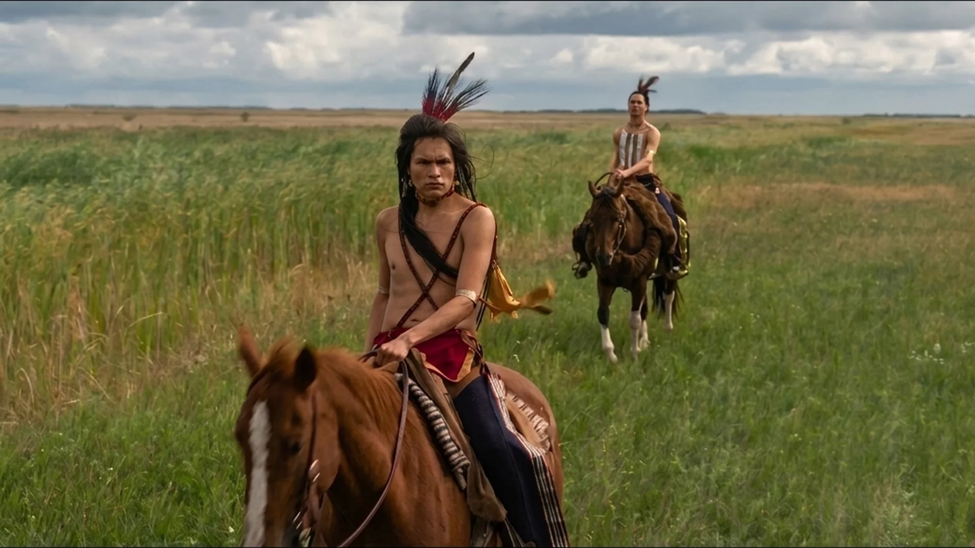 Two riders cross tall green grass on horseback in Little House on the Prairie.