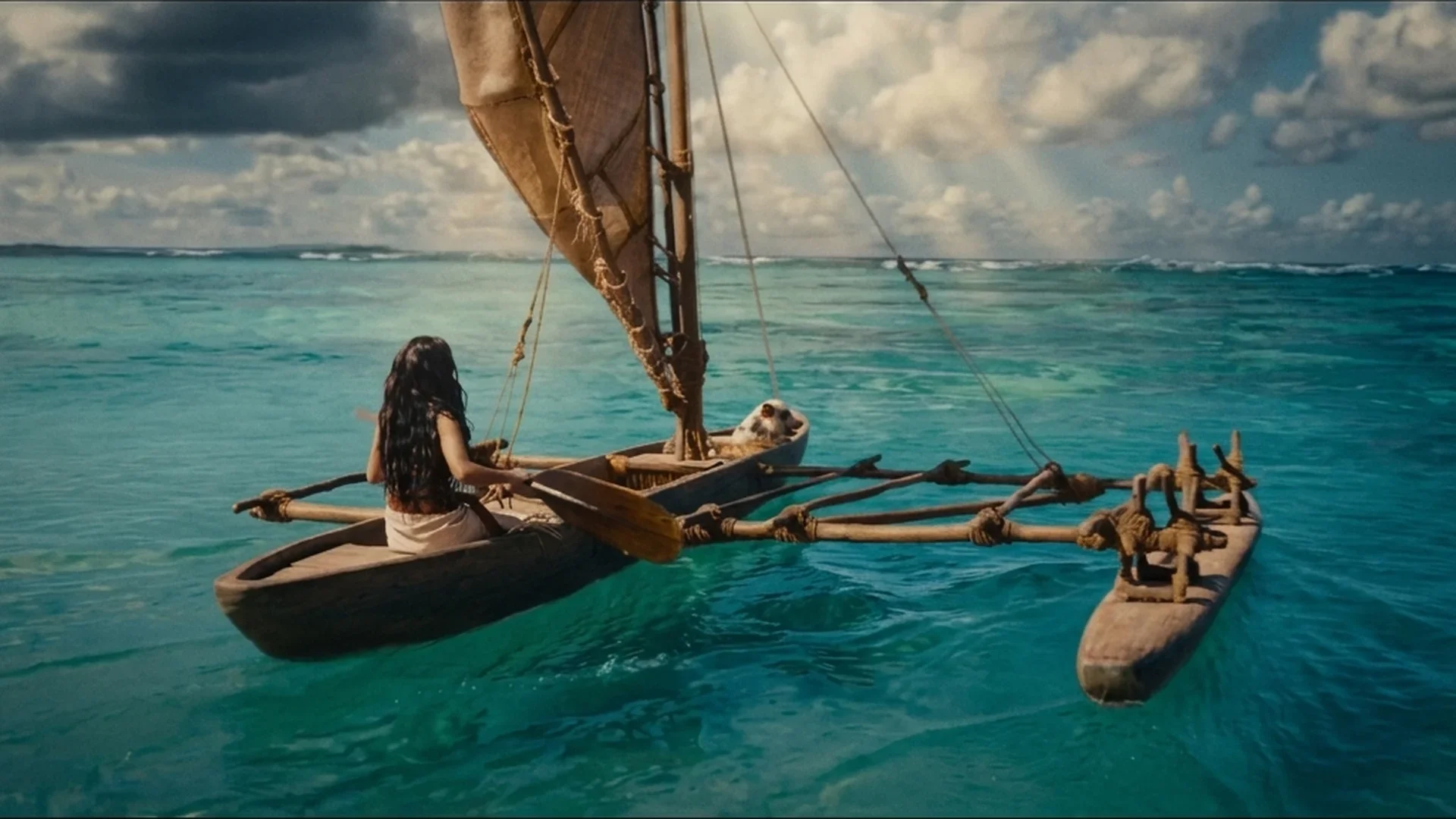 Catherine Laga'aia as Moana paddles her sailing canoe across turquoise water in Disney's live-action Moana