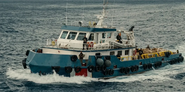 A crew boat cutting across open water in Mutiny, tires lashed along its hull and men standing on deck