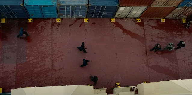 Looking straight down onto a cargo ship's red deck in Mutiny, stacked containers along one edge and crew scattered across the open steel