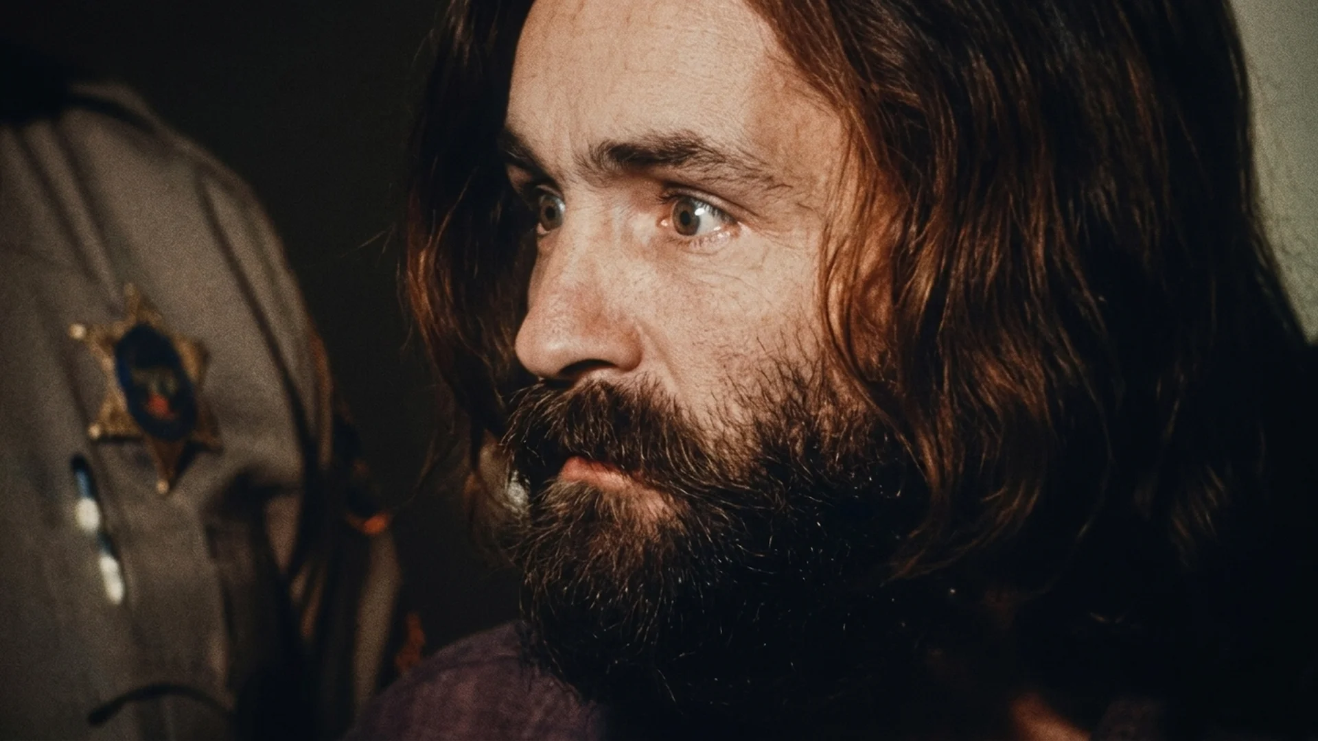Archival footage of a young, bearded Charles Manson looking to the side