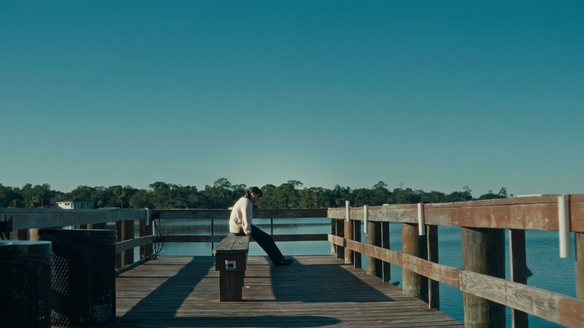 Sophia Maddox sits alone on a bench at the end of a wooden pier over still water