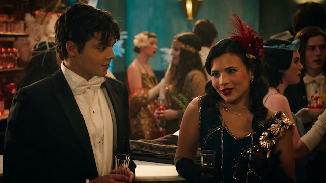 Jackie talks with a young man in a tuxedo at a 1920s-themed party.