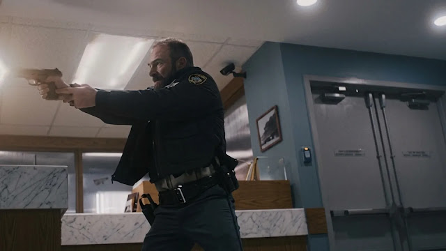 A man in a dark jacket firing a handgun inside a building