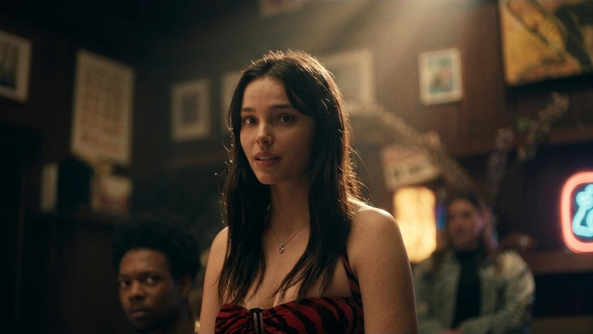 Nikki (Inde Navarrette) standing in a dim, neon-lit bar in the Obsession trailer