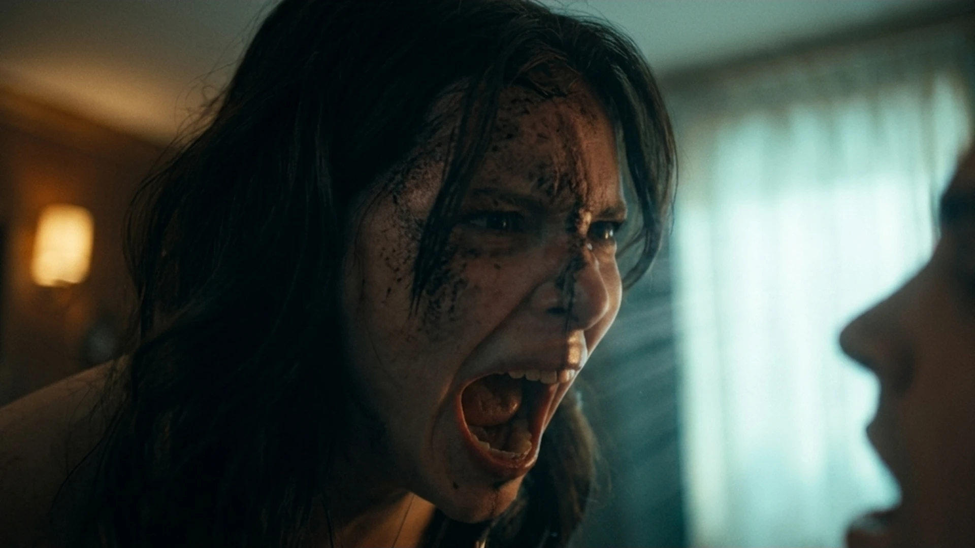 A woman screaming in rage at close range in a dim room in the Obsession trailer