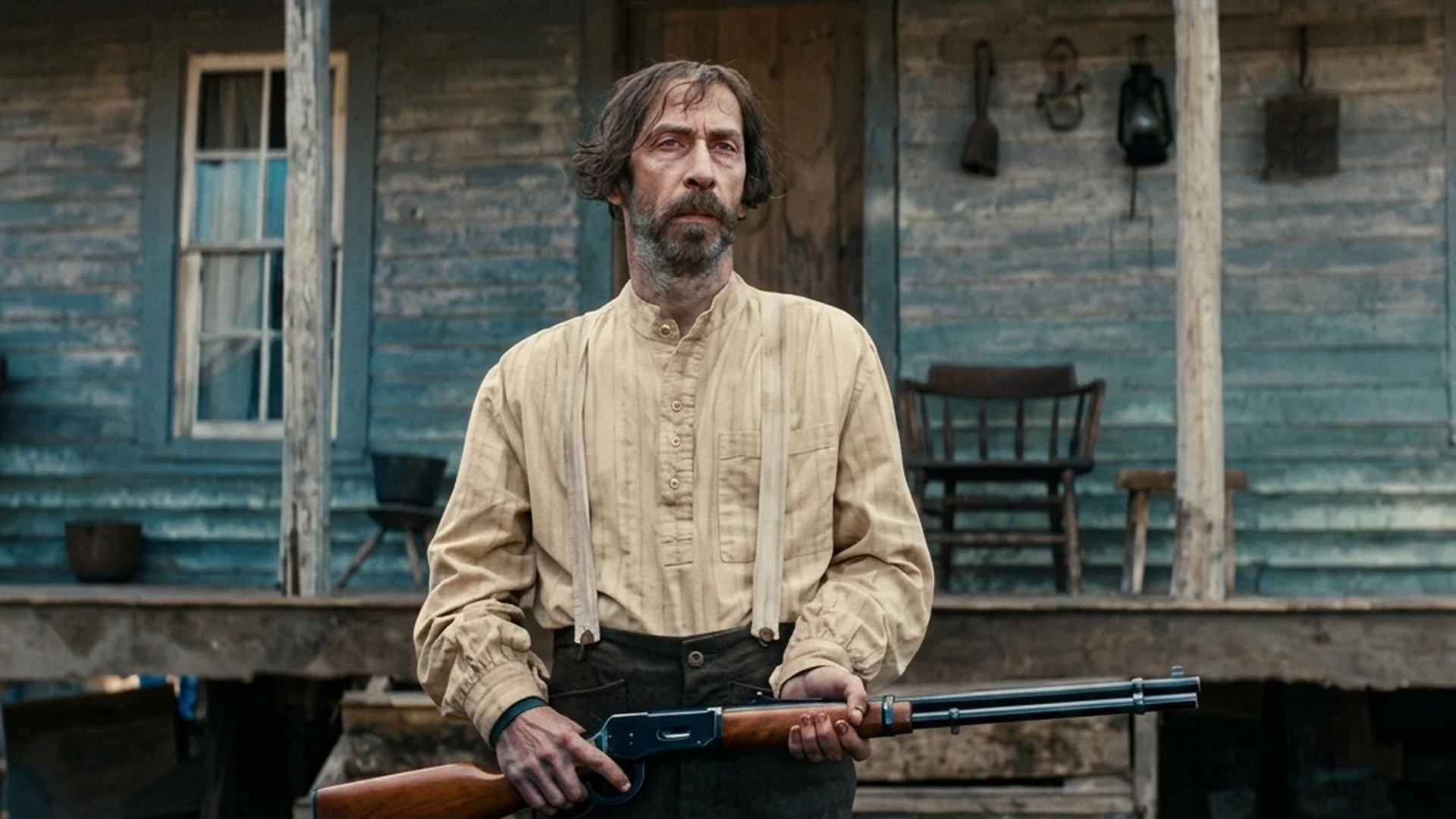 Tim Blake Nelson as Henry standing on his farmhouse porch holding a lever-action rifle in the Old Henry trailer