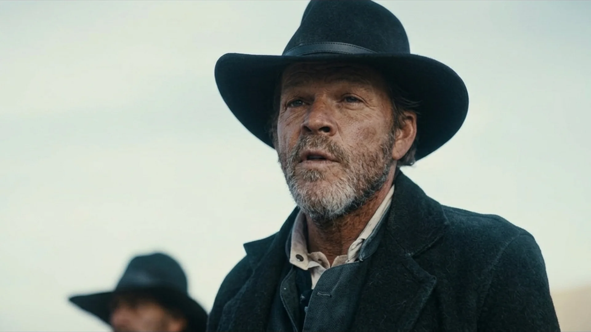A bearded man in a black hat and dark coat during the standoff at Henry's farm in the Old Henry trailer