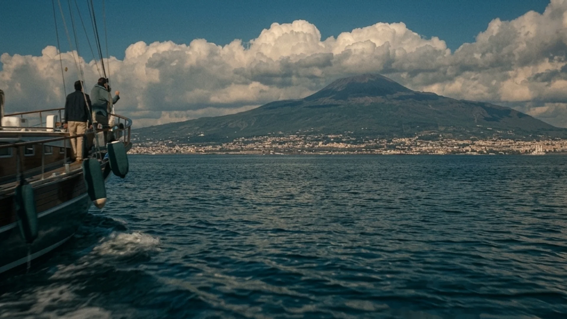 A boat crosses the Bay of Naples with Mount Vesuvius in the distance