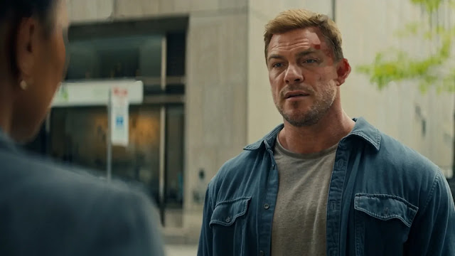 Alan Ritchson as Jack Reacher standing on a city street in Reacher Season 4