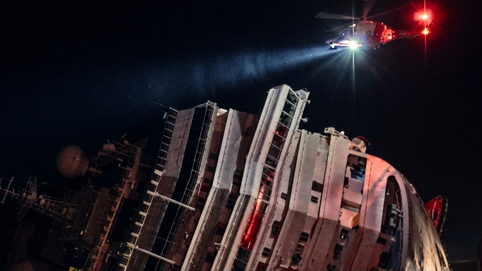 A helicopter searchlight over the capsized Costa Concordia at night in Netflix's Shipwrecked: Nightmare at Sea