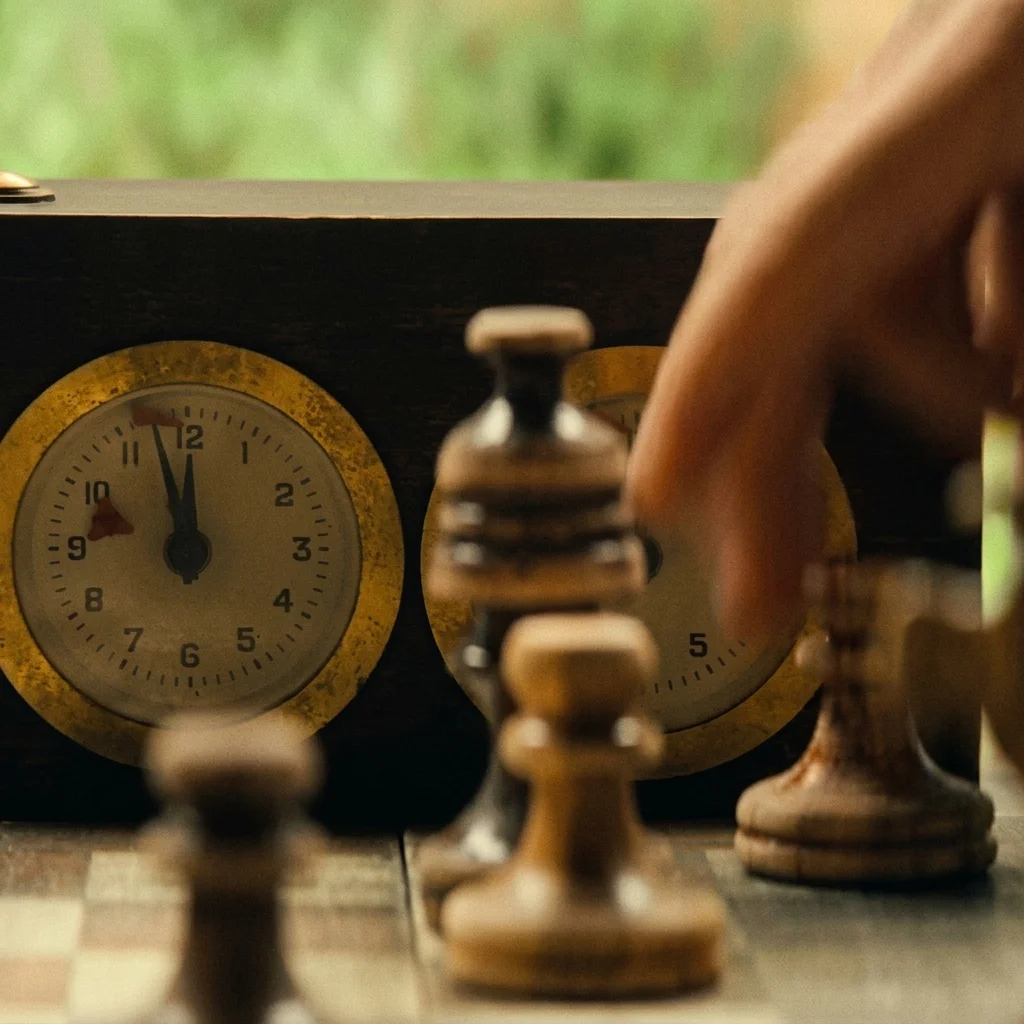 A chess board mid-game with an old timer clock, a hand moving a piece, the bomb-rigged match from The Agency's finale