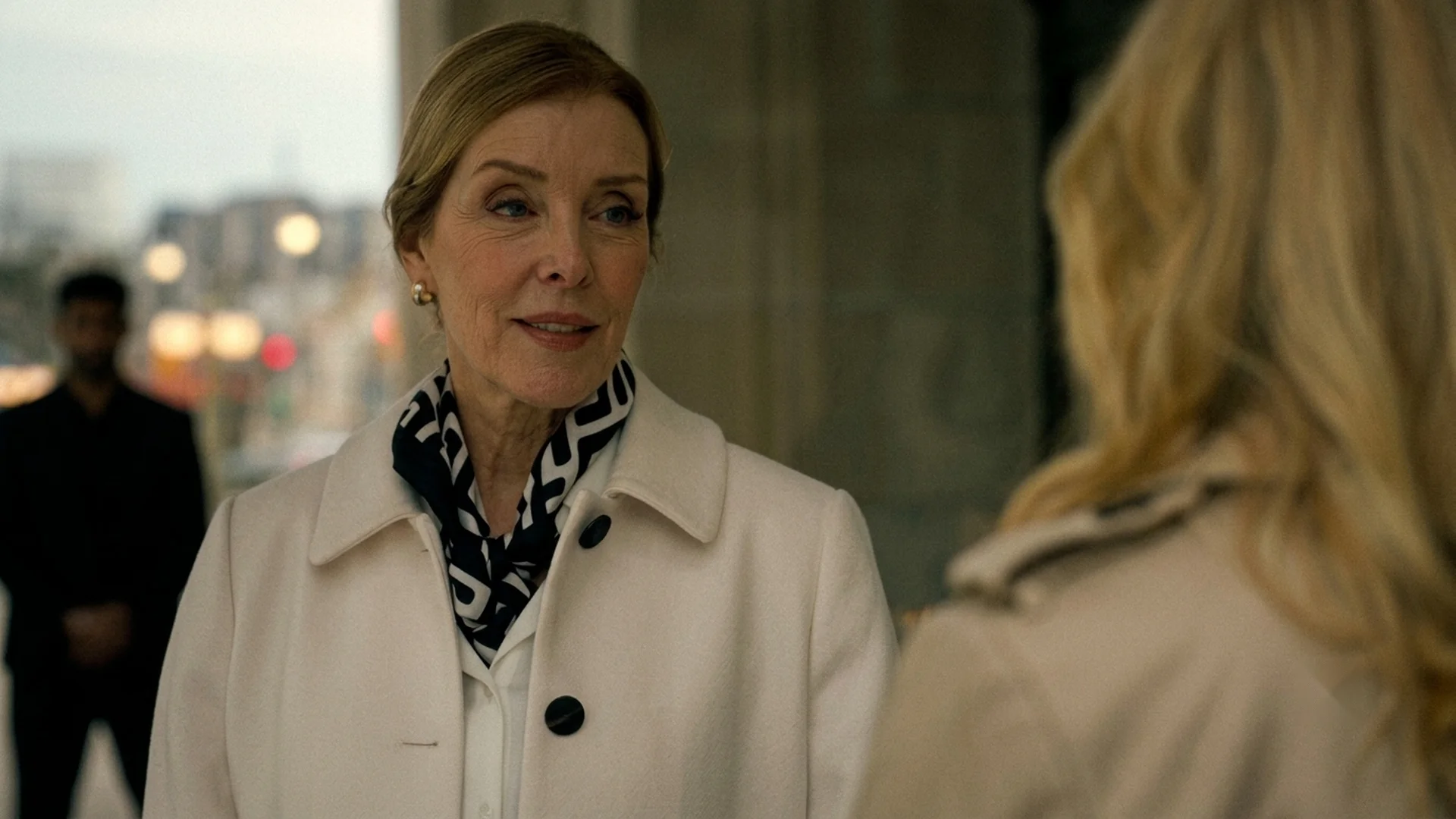 Clare, Amy's mother, faces the camera in a cream coat mid-conversation in The Body in the Locker