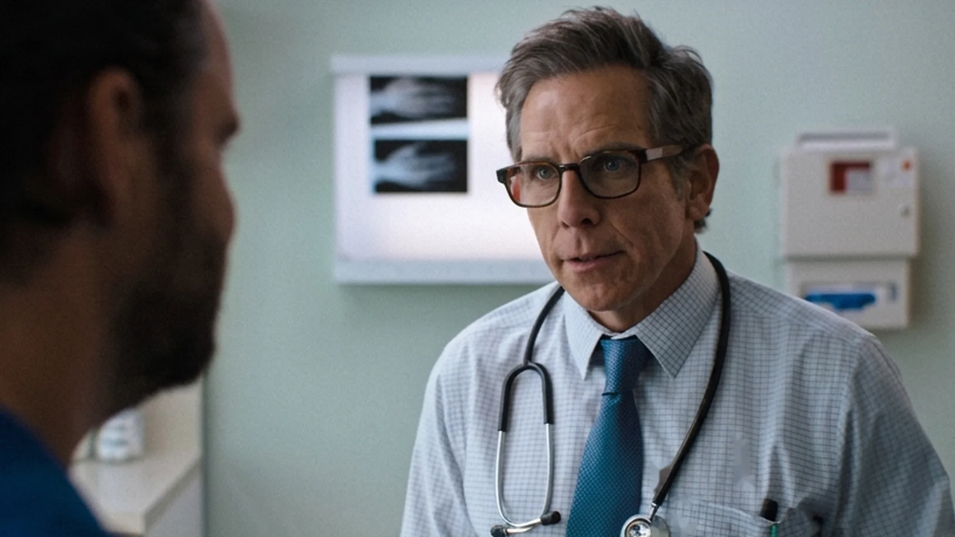 Ben Stiller, in glasses and a stethoscope, plays a doctor talking with a patient in an exam room.