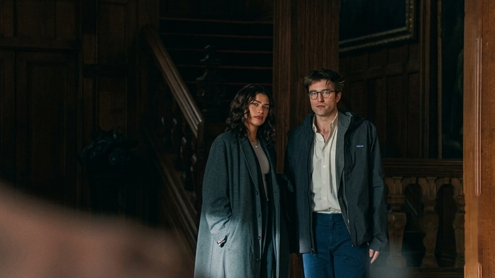Emma (Zendaya) and Charlie (Robert Pattinson) stand together in a dark wood-paneled interior in The Drama