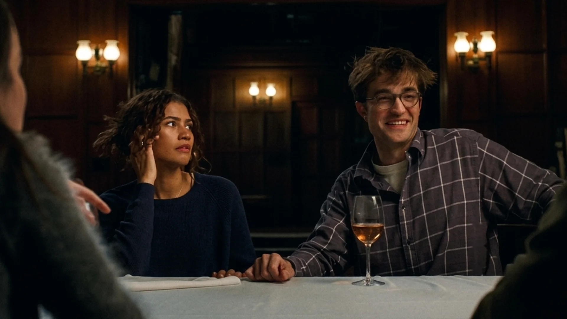 Emma (Zendaya) and Charlie (Robert Pattinson) sit at a table, Charlie smiling, in The Drama
