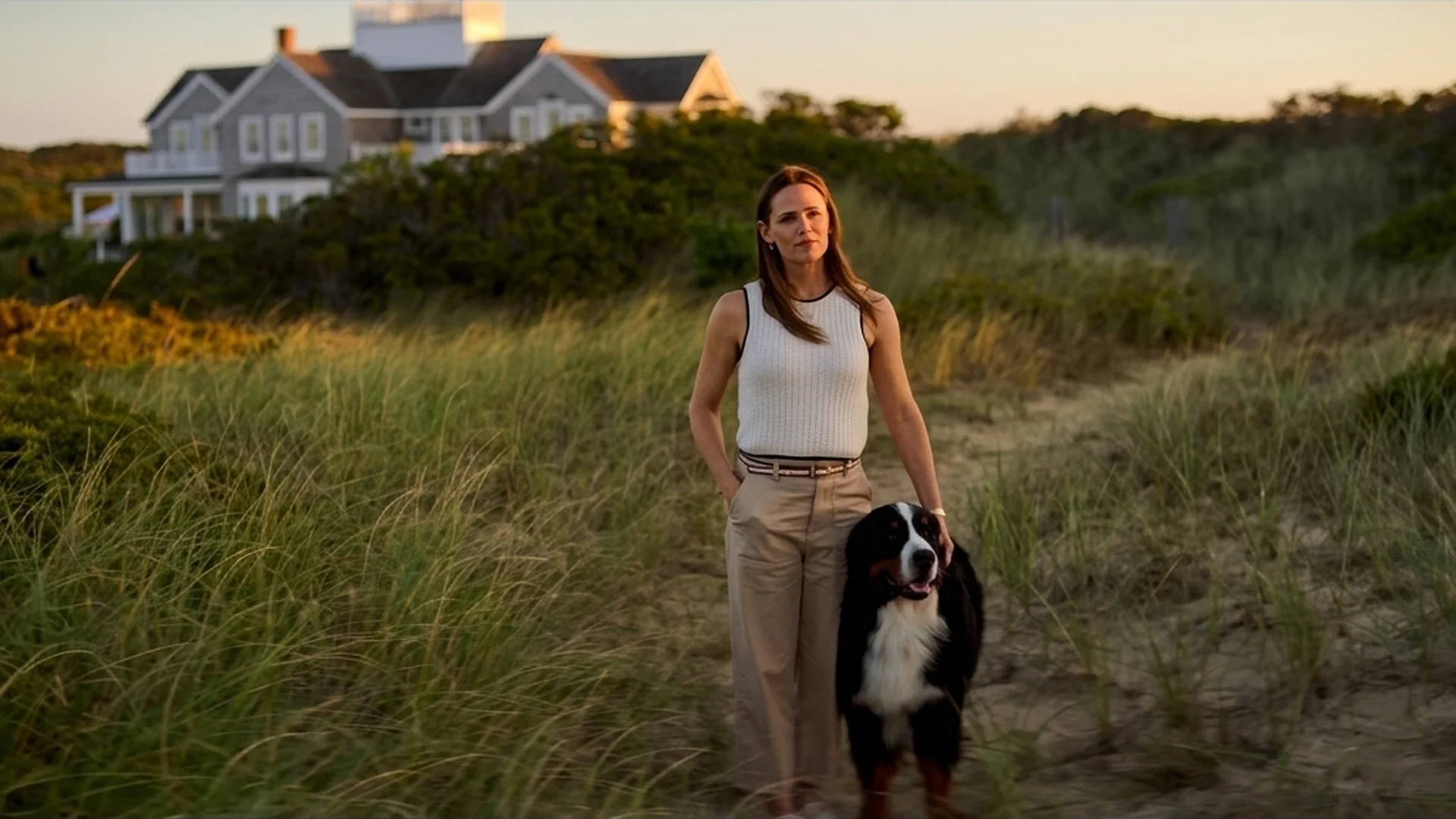 Hollis (Jennifer Garner) walking through golden dune grass with her dog, her Nantucket house behind her, in The Five Star Weekend