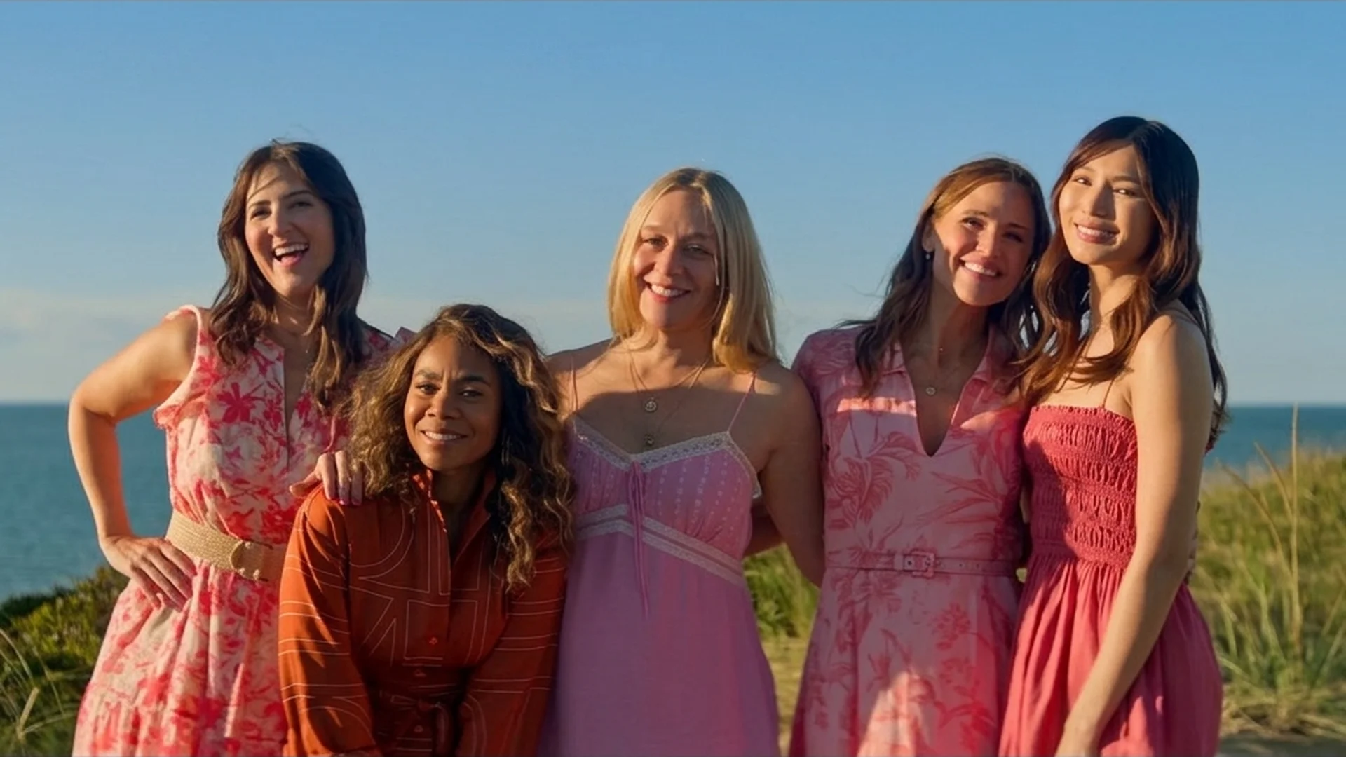 The five friends in matching pink summer dresses standing together on a Nantucket dune with the ocean behind them