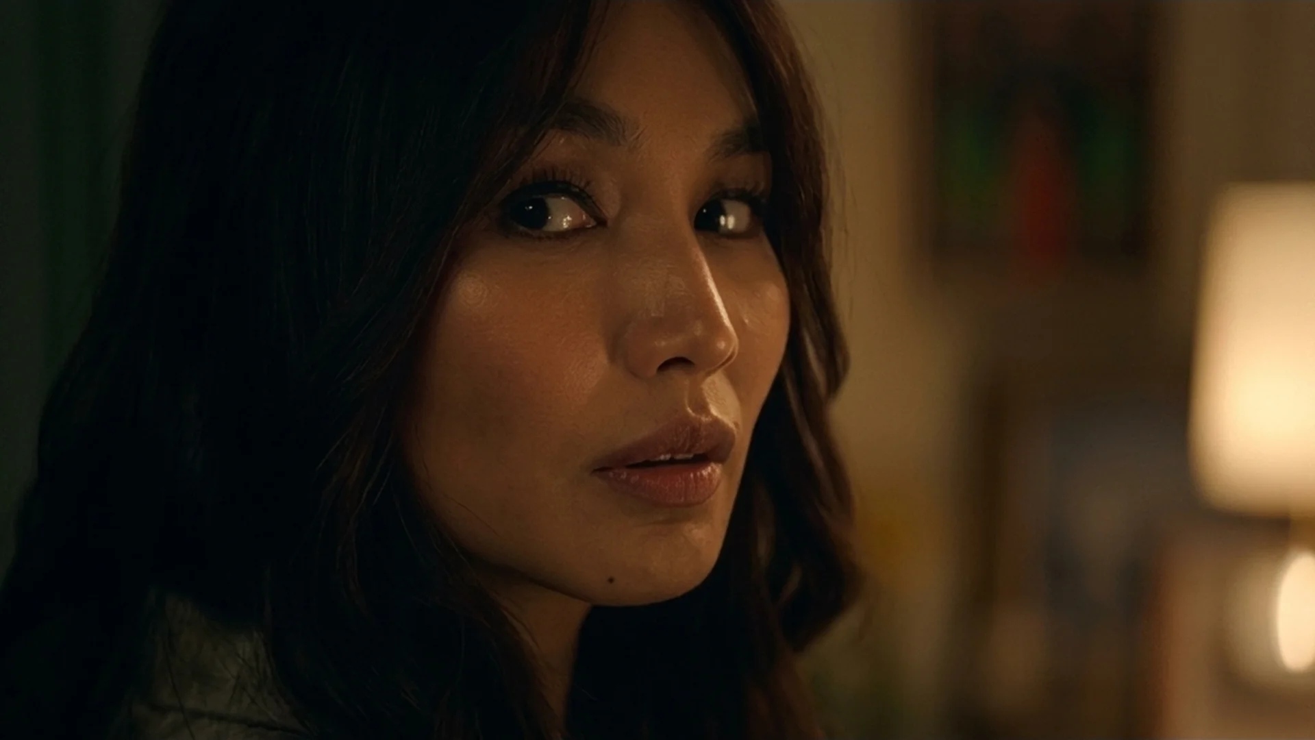Gigi (Gemma Chan) in warm lamplight with a guarded, searching look in The Five Star Weekend