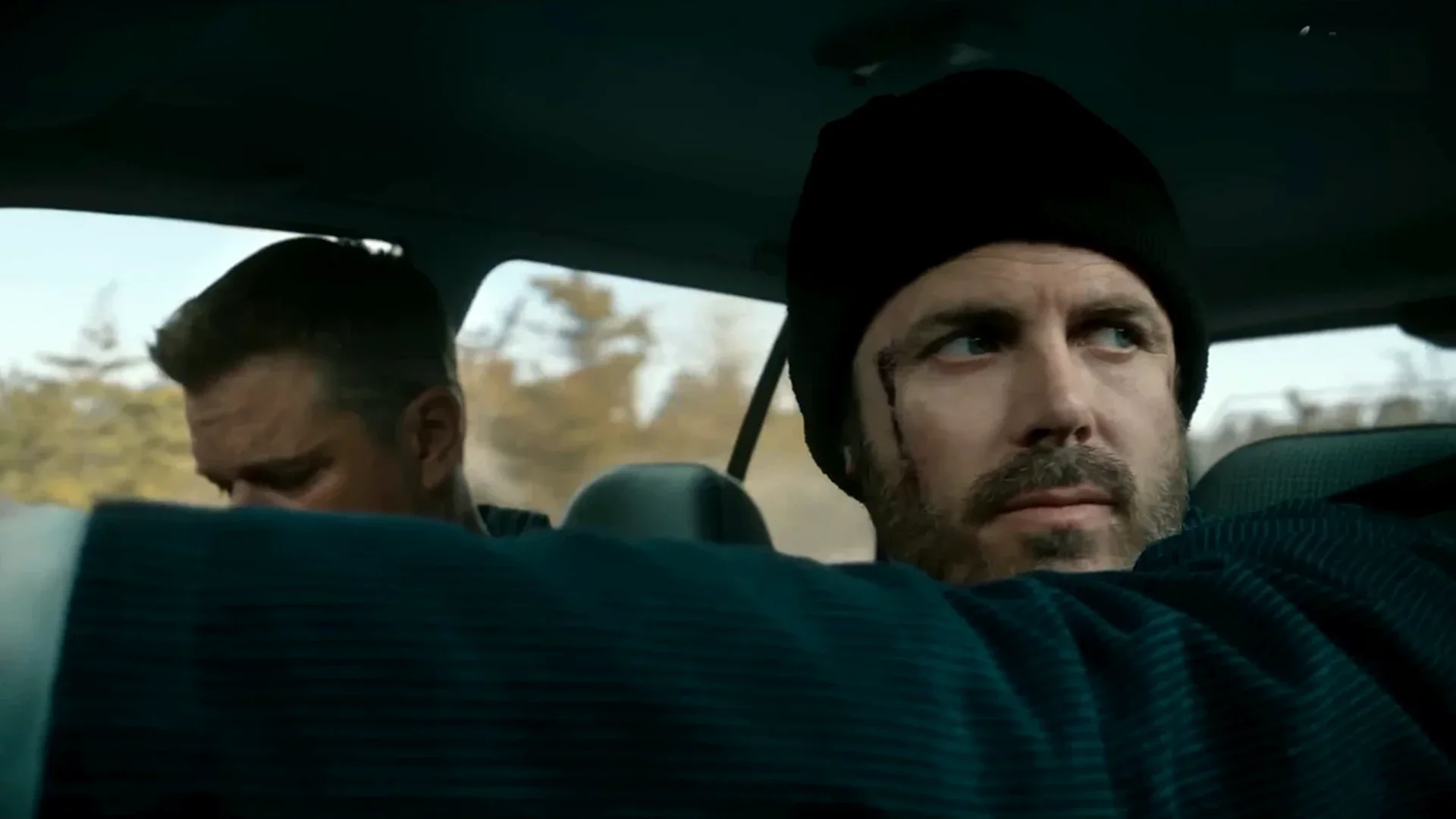 Cobby (Casey Affleck) drives as Rory (Matt Damon) leans in from the back seat in The Instigators