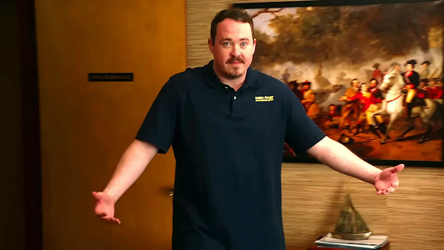 Shane Gillis as Shane, in a Valley Forge polo with his arms open, in an office in Tires Season 3