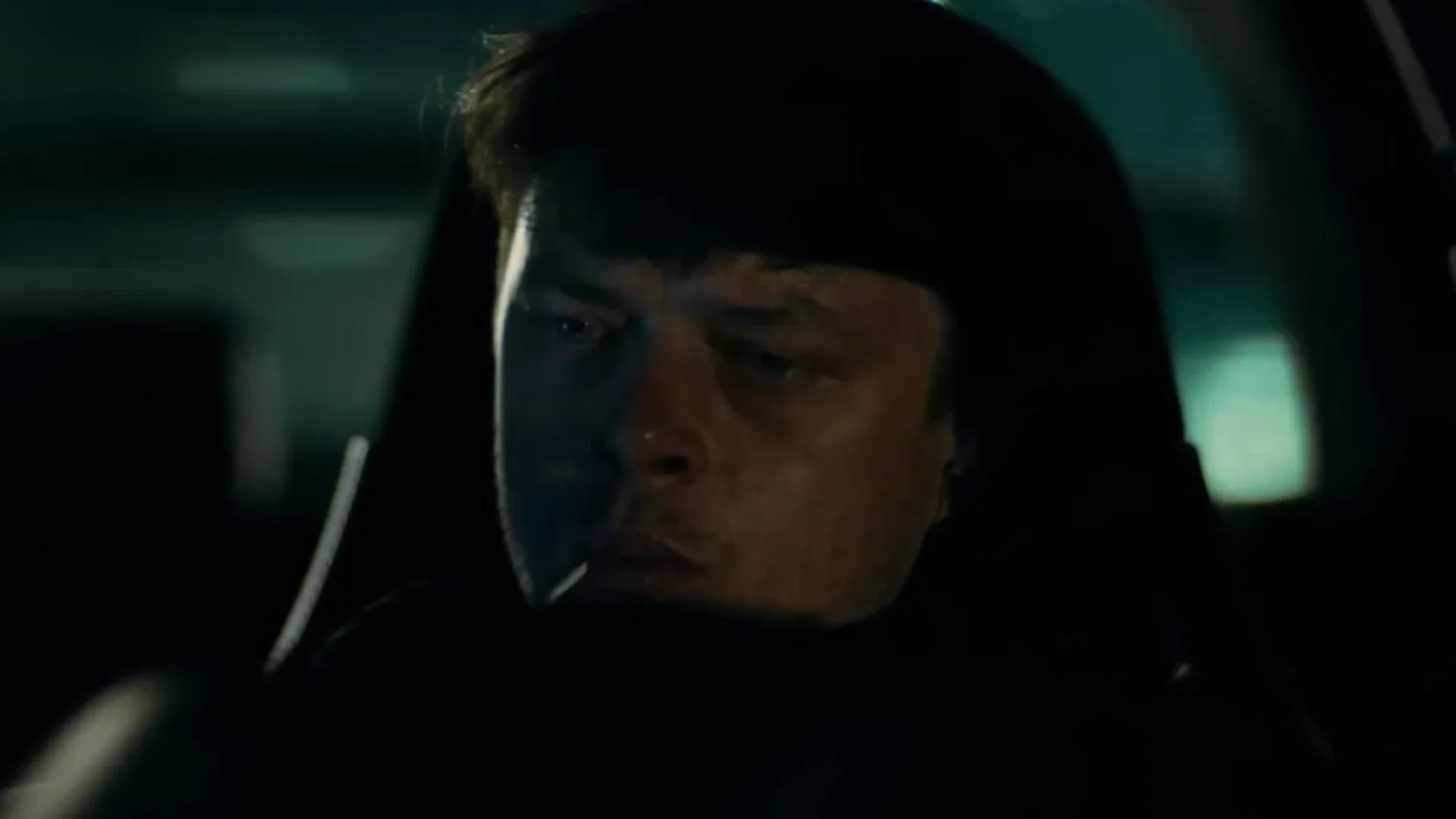 Dane DeHaan as Cole sits alone in a parked car at night, his face dimly lit, in Wardriver